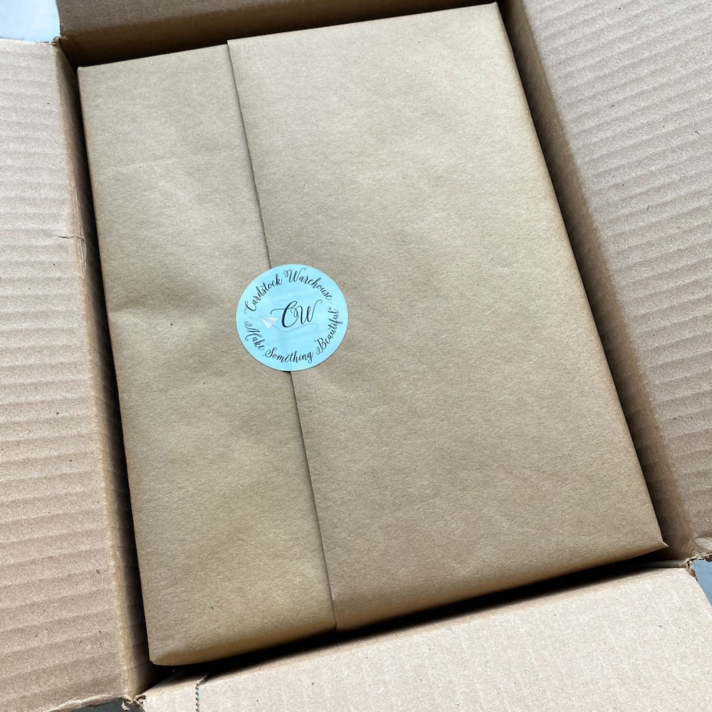 packs of paper wrapped in brown kraft paper with a cardstock warehouse sticker, inside a cardboard box.