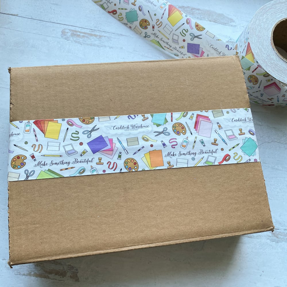 Illustrated packing tape stuck to brown cardboard box with a roll of tape
